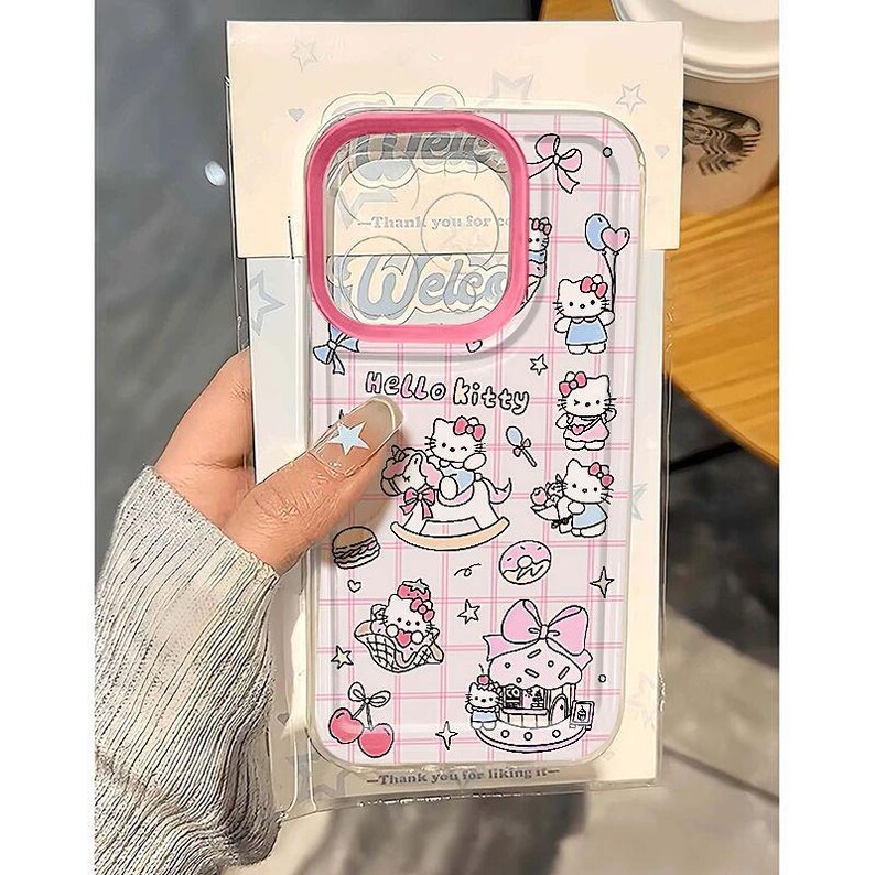Puede incluir: Funda transparente para tel&eacute;fono con borde rosa, decorada con personajes de Hello Kitty e ilustraciones tem&aacute;ticas. La funda tiene un patr&oacute;n de cuadr&iacute;cula e incluye el texto "Hello Kitty" y "Welcome".