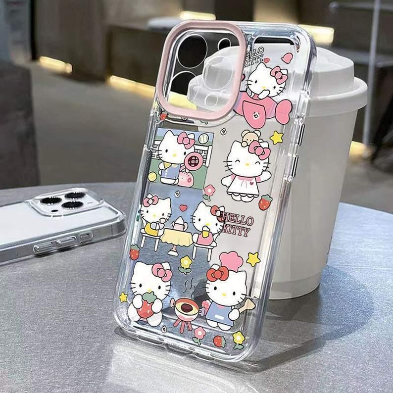 May include: Clear phone case featuring a pink and white Hello Kitty design. The case has a pink border around the camera and a repeating pattern of Hello Kitty characters in various poses, along with strawberries and stars.