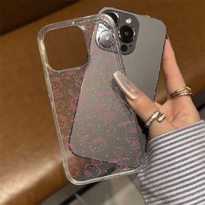 K&ouml;nnte beinhalten: Transparente Handyh&uuml;lle mit einem rosa Hello Kitty Muster und Glitzer. Das Design zeigt Hello Kitty Gesichter, Schleifen und Herzen. Die H&uuml;lle ist transparent, so dass die Farbe des Telefons durchscheint.