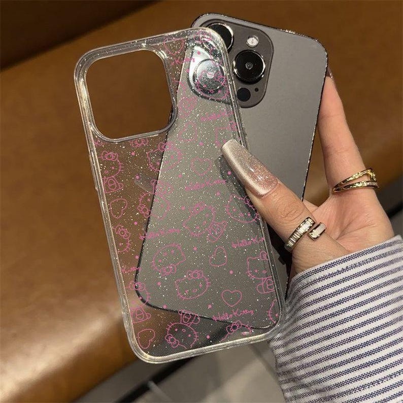 K&ouml;nnte beinhalten: Transparente Handyh&uuml;lle mit einem rosa Hello Kitty Muster und Glitzer. Das Design zeigt Hello Kitty Gesichter, Schleifen und Herzen. Die H&uuml;lle ist transparent, so dass die Farbe des Telefons durchscheint.