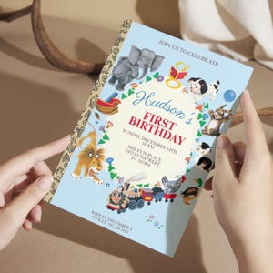 Puede incluir: Una tarjeta de invitaci&oacute;n azul claro para una celebraci&oacute;n de primer cumplea&ntilde;os. La tarjeta presenta ilustraciones de animales, un tren y el texto "Hudson's First Birthday". La invitaci&oacute;n incluye la fecha, hora y lugar.