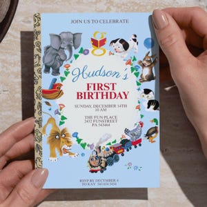 Puede incluir: Una invitaci&oacute;n de cumplea&ntilde;os azul claro con un dise&ntilde;o caprichoso. La invitaci&oacute;n presenta ilustraciones de animales, un tren y el texto "Hudson's First Birthday". La invitaci&oacute;n es sostenida por una persona.