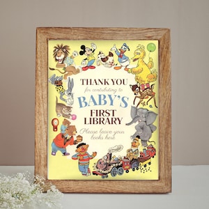 K&ouml;nnte beinhalten: Ein gerahmter Druck mit gelbem Hintergrund und einer Sammlung von Zeichentrickfiguren, die den Text "BABY'S FIRST LIBRARY" umgeben. Der Rahmen besteht aus hellbraunem Holz. Der Druck zeigt Figuren wie Mickey Mouse und Big Bird.