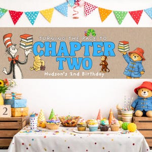 Op de afbeelding: Een verjaardagsbanner met de tekst "Turning the Page to Chapter Two" in blauw, met illustraties van kinderboekfiguren. De banner bevindt zich boven een tafel met cupcakes en feestversieringen.