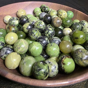 May include: A bowl filled with green and black serpentine spheres. The spheres are smooth and polished, and they have a variety of patterns and textures.