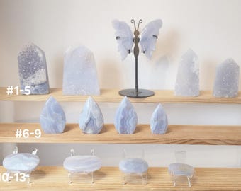 May include: A collection of blue lace agate crystals arranged on three wooden shelves. The crystals are in various shapes and sizes, including points, freeforms, and slabs. The shelves are labelled with numbers 1-5, 6-9, and 10-13.