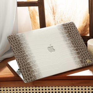 May include: A laptop with a white and brown faux crocodile skin case. The case has a gradient design, transitioning from brown to white. The Apple logo is visible on the laptop. The initials "IK" are on the bottom right corner.
