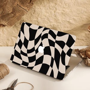 Puede incluir: Una piel para portátil a cuadros en blanco y negro con un patrón ondulado. La piel se aplica a un portátil plateado.