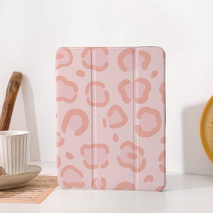 Può includere: Una custodia per tablet rosa con un design a stampa leopardata rosa chiaro e pesca.