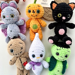 May include: A selection of handmade crochet Halloween dolls. The dolls include a grey bat, orange pumpkin, black cat, tan doll, white ghost, and green Frankenstein. Each doll has large eyes and unique details.