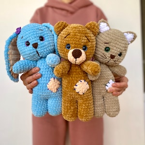 May include: Three crocheted stuffed animals: a blue bunny, a brown bear, and a gray cat. Each animal has embroidered eyes and a stitched nose.
