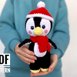 May include: Crochet penguin amigurumi pattern in PDF format. The penguin is wearing a red and white Santa hat and a red scarf.