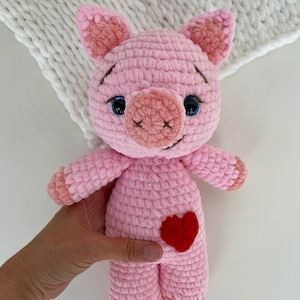 Op de afbeelding: Een roze gehaakt varkenspeelgoed met een rood hartje op zijn buik. Het varken heeft zwarte ogen en een bruine neus.
