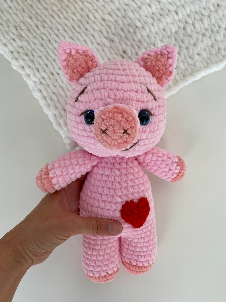 Op de afbeelding: Een roze gehaakt varkenspeelgoed met een rood hartje op zijn buik. Het varken heeft zwarte ogen en een bruine neus.