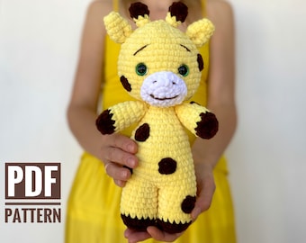 May include: A crocheted giraffe toy with brown spots, yellow fur, and green eyes. The giraffe is being held by a person wearing a yellow dress.