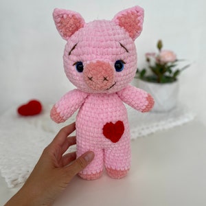 Op de afbeelding: Roze gehaakt knuffel varken met blauwe ogen en een rood hartje op zijn buik.