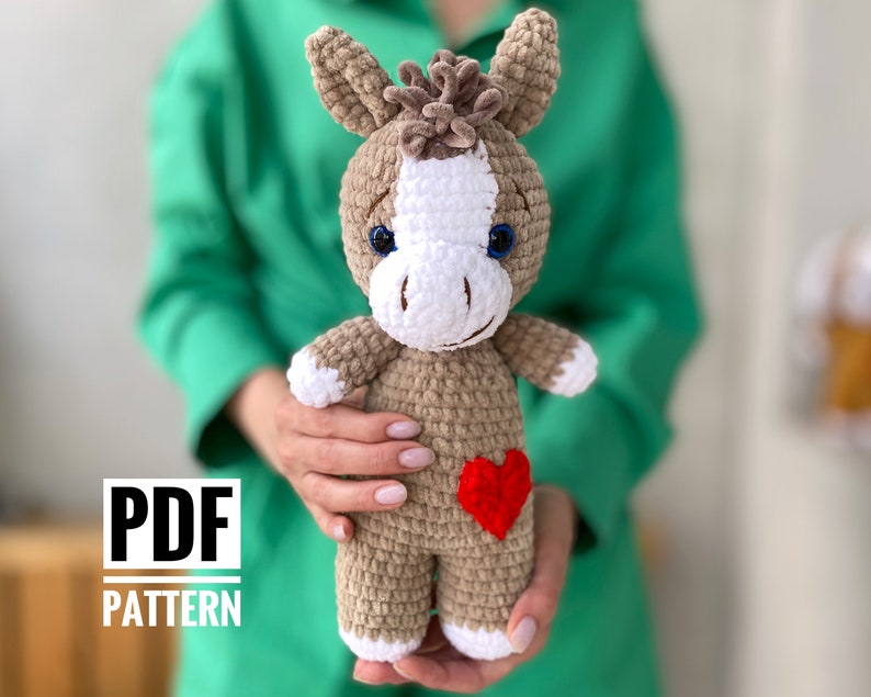 Op de afbeelding: Haakpatroon voor een amigurumi-ezel in PDF-formaat. Het patroon bevat instructies voor het haken van een bruine en witte ezel met blauwe ogen en een rood hart op zijn borst.