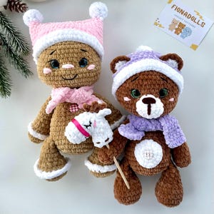 May include: Two crocheted plush toys: a gingerbread man and a bear. The gingerbread man wears a pink hat and scarf, holding a white horse. The bear has a purple hat and scarf, holding a wooden stick. The toys are handmade.