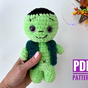 May include: Green crochet Frankenstein monster amigurumi toy with black hair and a green vest. The toy has pink eyes and a stitched-on smile. The text "PDF PATTERN" is in the lower right corner of the image.