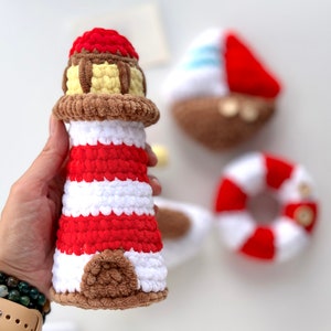 May include: A crocheted lighthouse toy with red and white stripes, a brown roof, and a yellow window. The lighthouse is held in a hand with a green bracelet.