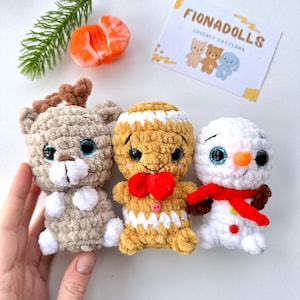 Op de afbeelding: Drie handgemaakte gehaakte poppen: een rendier, een peperkoekmannetje en een sneeuwpop. Het rendier is bruin met bruine geweien, het peperkoekmannetje is bruin met witte glazuur en de sneeuwpop is wit met een rode sjaal. De poppen hebben grote, expressieve ogen. De kaart leest "FIONADOLLS CROCHET PATTERNS".