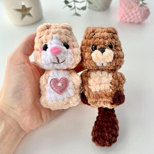 May include: Two crocheted stuffed animals, one brown and one beige, with a pink heart on the beige animal. The animals are both holding a heart-shaped object.