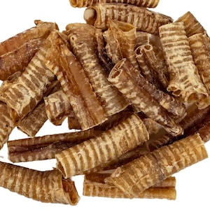 Può includere: Un mucchio di snack per cani essiccati, marrone chiaro, ciascuno con una consistenza a coste e un centro cavo. Gli snack sono sparsi su uno sfondo bianco, mostrando il loro colore e la loro forma naturali. Questi sono probabilmente uno spuntino sano per animali domestici.