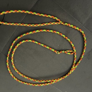 May include: A patterned dog lead with a looped handle and a clasp. The lead is made of a durable, woven rope in a pattern of orange, yellow, and black. A small tag is attached to the handle.