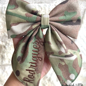 Peut inclure: N&oelig;ud papillon &agrave; motif camouflage vert, marron et beige. Le nom "Rodriguez" est brod&eacute; en fil marron. Le texte "the Awkward Little turtle" est imprim&eacute; en noir en bas &agrave; droite.