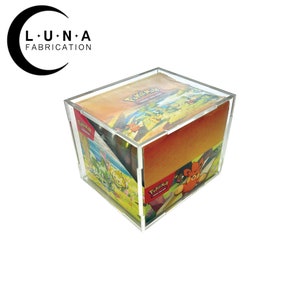 May include: A clear acrylic display case with a lid, showcasing a collection of Pokémon Trading Card Game cards. The cards are visible through the transparent sides, with colorful artwork and the Pokémon logo. The case is square and sits on a white surface.