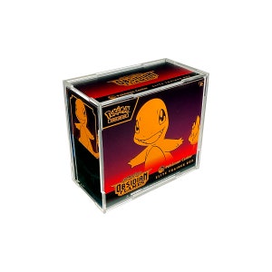 May include: A clear acrylic display case holding a Pokémon Center Elite Trainer Box. The box features a smiling orange Charmander on a dark background with the text "Obsidian Flames" and "Pokémon".