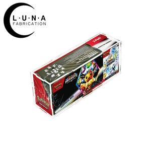 May include: A clear acrylic box containing a Pokemon Prismatic Evolutions Surprise Box. The box features a 2-pack booster bundle with colorful graphics of Pokemon characters. The Luna Fabrication logo is in the upper left corner.