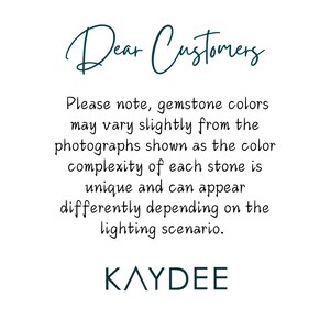 Op de afbeelding: Witte achtergrond met tekst in een turquoise scriptletter die "Dear Customers" luidt. Hieronder staat dat de kleuren van edelstenen enigszins kunnen afwijken van de foto's vanwege de unieke kleurcomplexiteit van elke steen en de belichting. De merknaam "KAYDEE" staat onderaan.