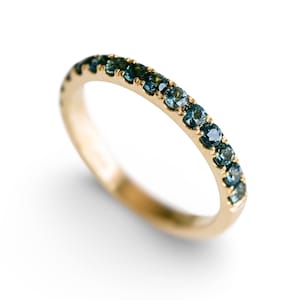 Puede incluir: Un anillo de banda de oro con una fila de piedras preciosas azules engastadas alrededor de toda la banda.