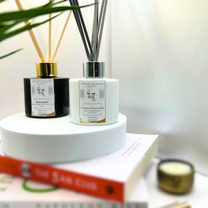 Può includere: Due diffusori di canna in vetro nero e bianco con tappi dorati e argentati. I diffusori sono etichettati "Bouquet" e "Tropical Paradise" con il marchio "Oshun Scents by SOW".
