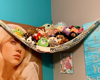 May include: A colorful hammock filled with stuffed animals hangs from the corner of a room. The wall behind the hammock is painted a light blue color. A poster of a young woman with blonde hair is on the wall behind the hammock. The wall to the right of the hammock has a blue and white canvas with the text "Don't Let Anyone Dull Your Spark" written on it.