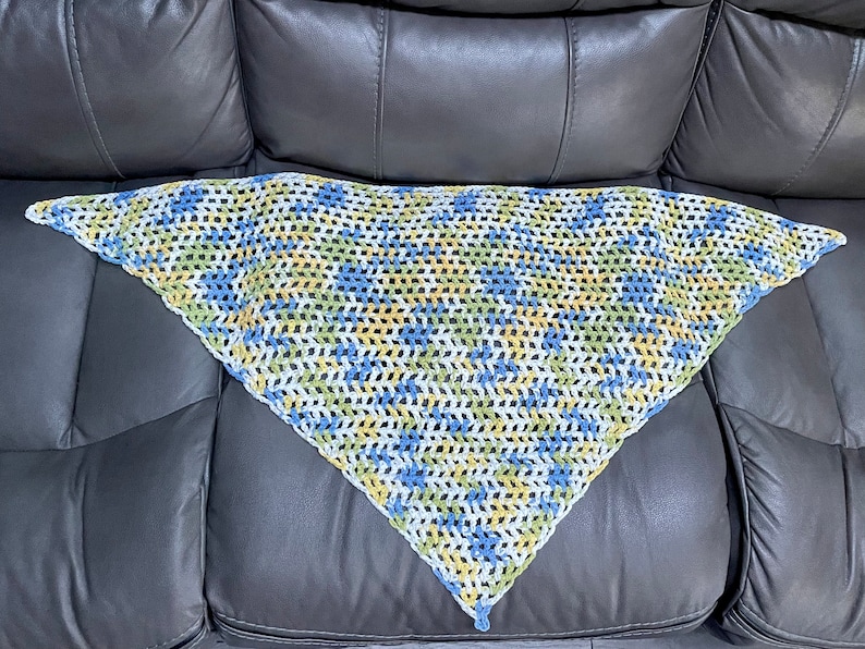 May include: A triangular crocheted shawl in white, blue, and yellow.
