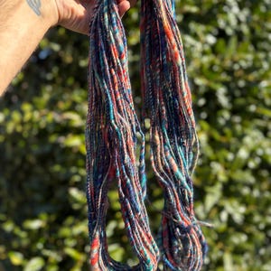 May include: A skein of colorful yarn with shades of blue, red, orange, and white. The yarn is made of wool and is perfect for knitting or crocheting.