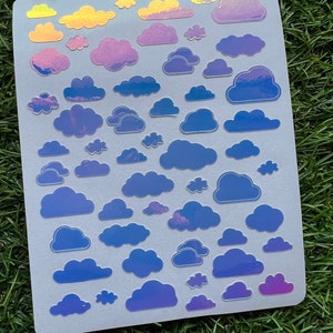 May include: A sheet of iridescent holographic stickers featuring various sizes and shapes of clouds. The clouds are in shades of blue, purple, and yellow.