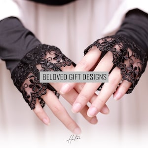 May include: Black fingerless gloves with intricate floral lace trim. The gloves are shown on a person's hands, with the text "BELOVED GIFT DESIGNS" overlaid on the image. The gloves are a stylish accessory.
