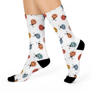 May include: A pair of white socks with a colorful ladybug pattern. The socks have black heels and toes.