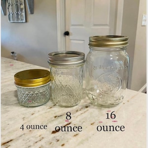 May include: Three glass jars with gold lids, labeled 4 ounce, 8 ounce, and 16 ounce. The jars are clear and have a textured surface.