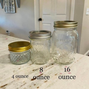 Three empty clear glass mason jars of different sizes are arranged on a surface, labeled 4 ounce, 8 ounce, and 16 ounce from left to right.