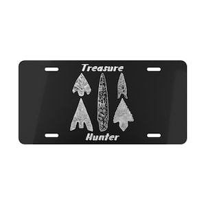 May include: Black license plate with white text and images. The text reads "Treasure Hunter" and there are five images of arrowheads.