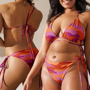 May include: A two-piece bikini set featuring a vibrant camouflage pattern in shades of orange, red, and purple. The top has triangle cups with thin tie straps, and the matching bikini bottom includes adjustable side ties for a customizable fit.