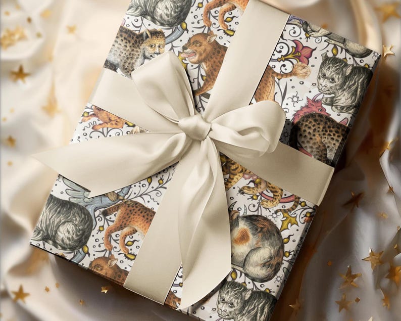 May include: A square gift box wrapped in patterned paper featuring illustrations of various cat-like creatures in shades of brown, gray, and cream. A cream-colored satin ribbon and bow adorn the top, creating a luxurious presentation.