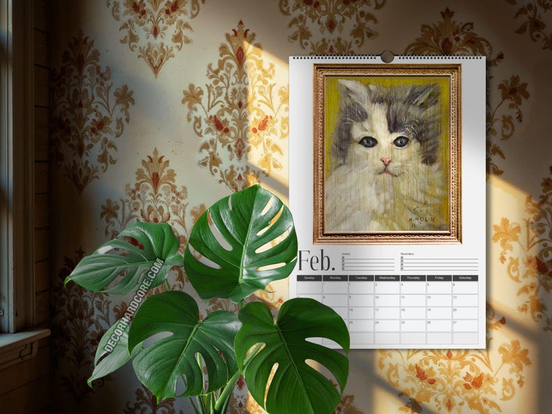 May include: A wall calendar for the month of February featuring a portrait of a fluffy cat with grey and white fur against a yellow background, enclosed in a gold-toned frame. The calendar includes a grid for dates and the text Feb. at the top.