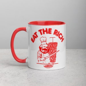 May include: White ceramic mug with a red rim and handle. The mug features a red illustration of a person in a chef's hat holding a knife and a large kebab. The text "EAT THE RICH" is written in red around the illustration.