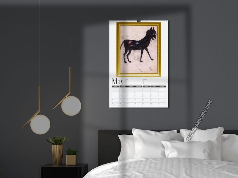 May include: A wall calendar for the month of May featuring a framed illustration of a black cat with small red and blue spots on its side. The calendar has a white background with a black grid for dates and the text May printed at the top.