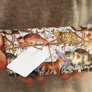 May include: A wrapped gift featuring a decorative paper with illustrations of various cats and felines, tied with twine and a blank white tag. The gift wrap has a cream background with colorful cat illustrations.